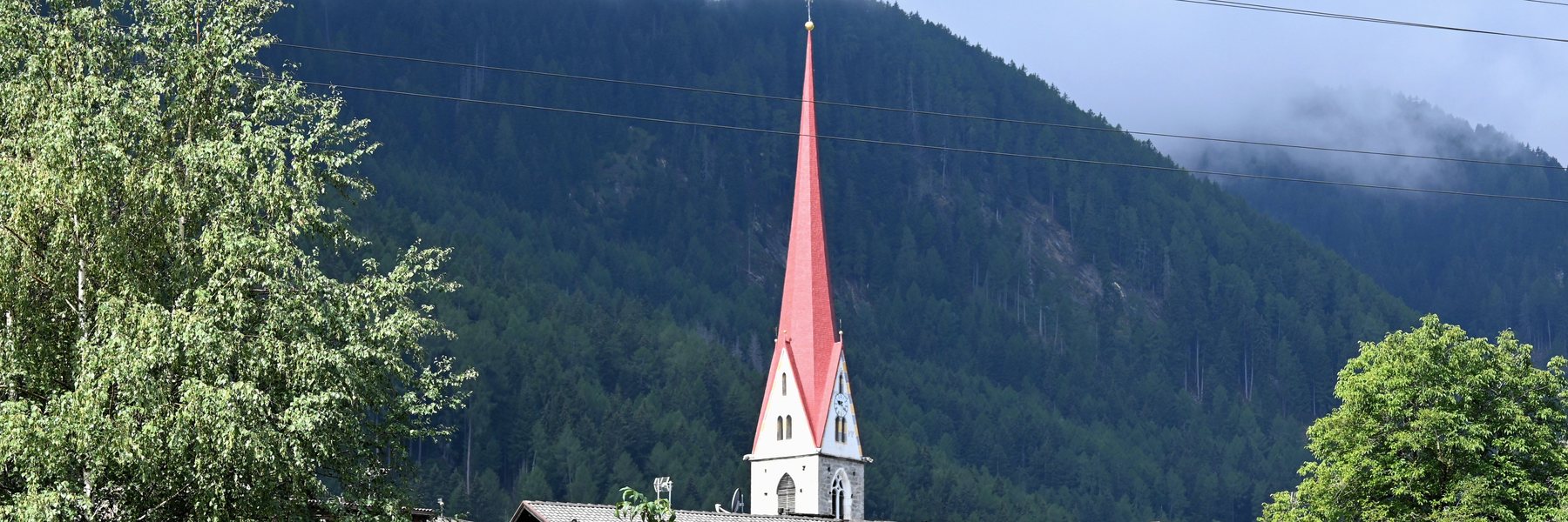 Österreichischer Ort mit Wohnhäusern und Kirchturm vor bewaldetem Hang