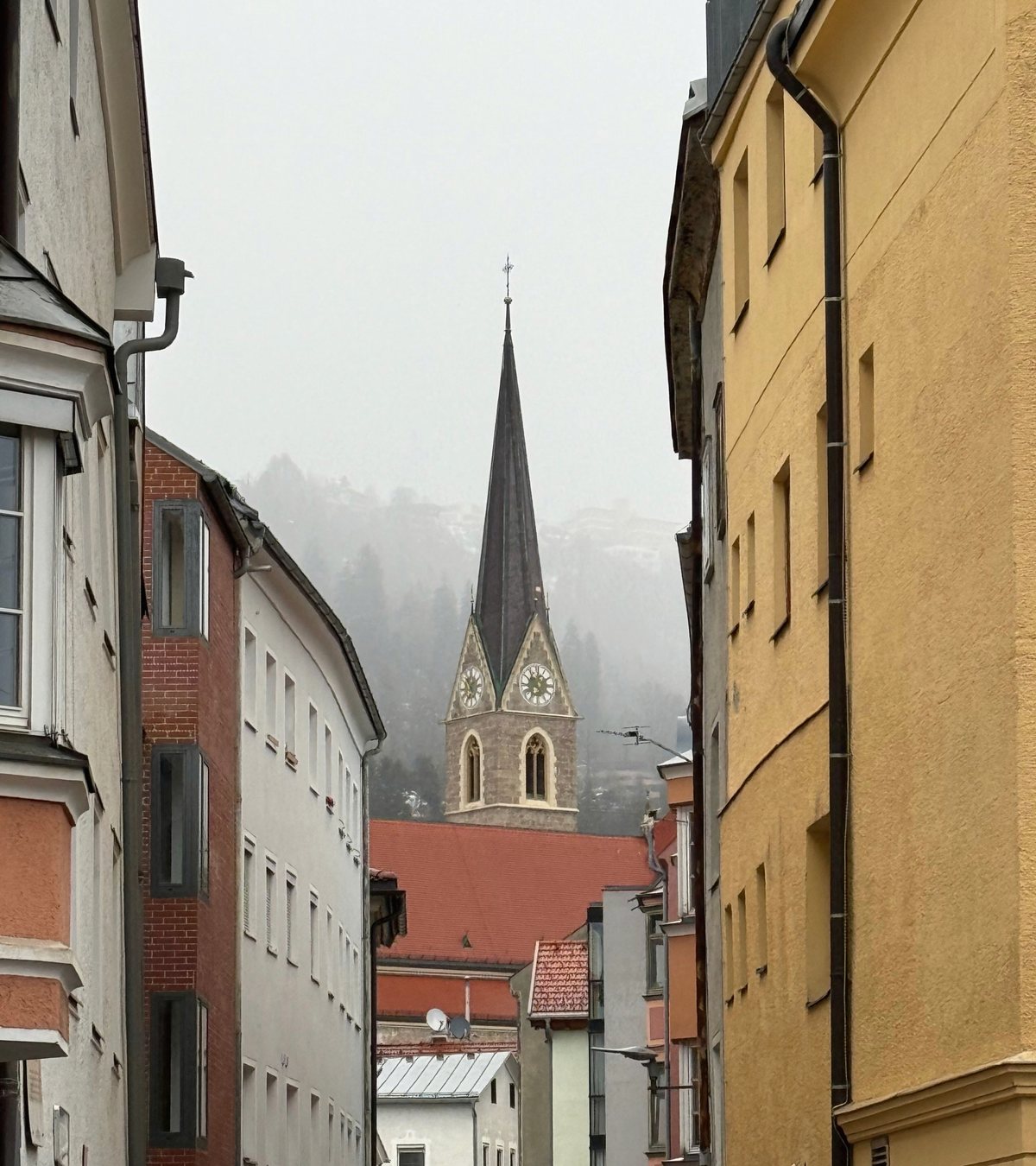 Gasse mit Wohnhäusern und sichtbarem Kirchturm in einer österreichischen Stadt