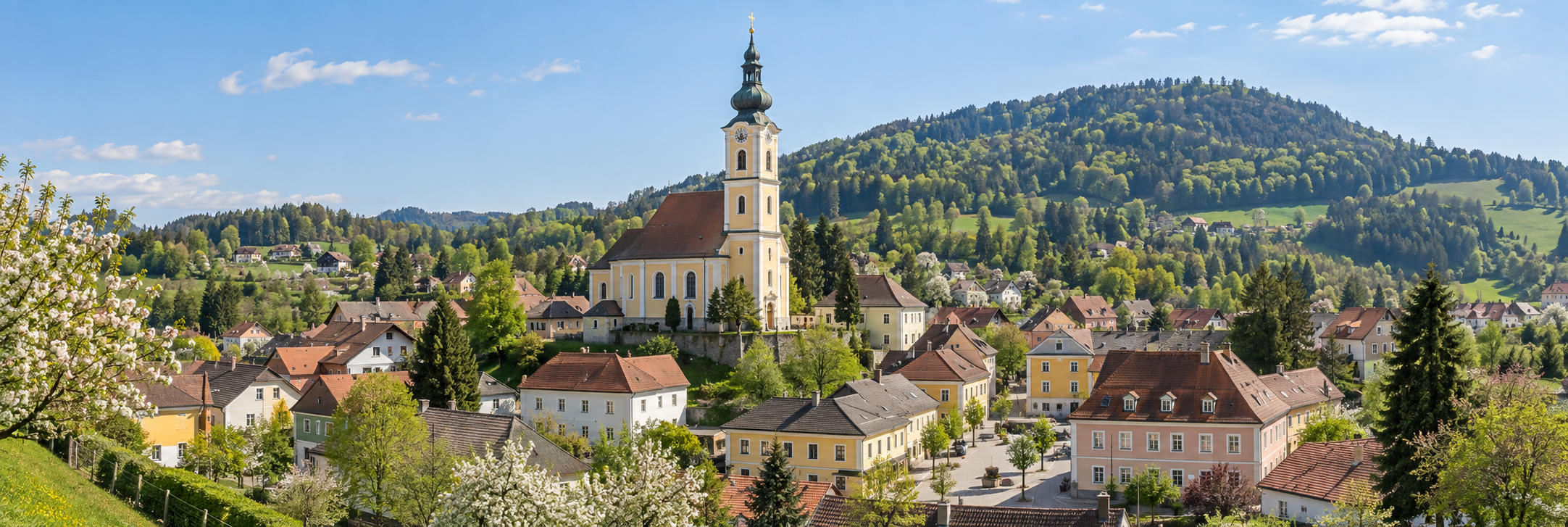 Österreichischer Ort mit Wohnhäusern und Kirchturm vor bewaldetem Hang